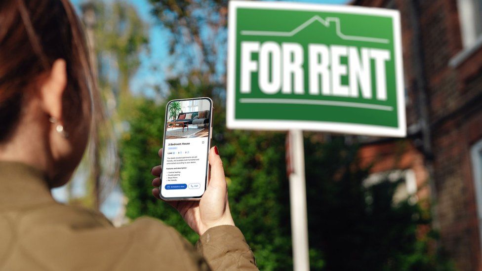 Woman looking at picture on phone outside building with For Rent sign