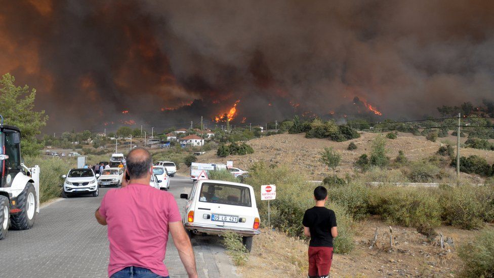 Two men look towards a hillside on fire in Turkey