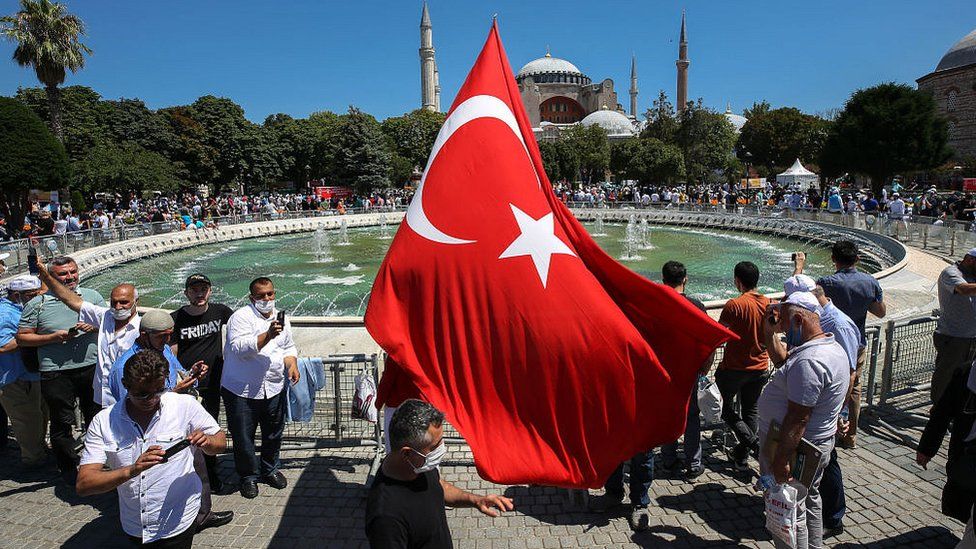 A man waves a Turkish flag as people gather around the Hagia Sophia Mosque ahead of Friday prayer, performed for the first time in 86 years on July 24, 2020 in Istanbul
