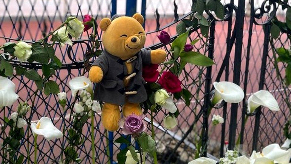 A bear hangs on a fence with white lillies below