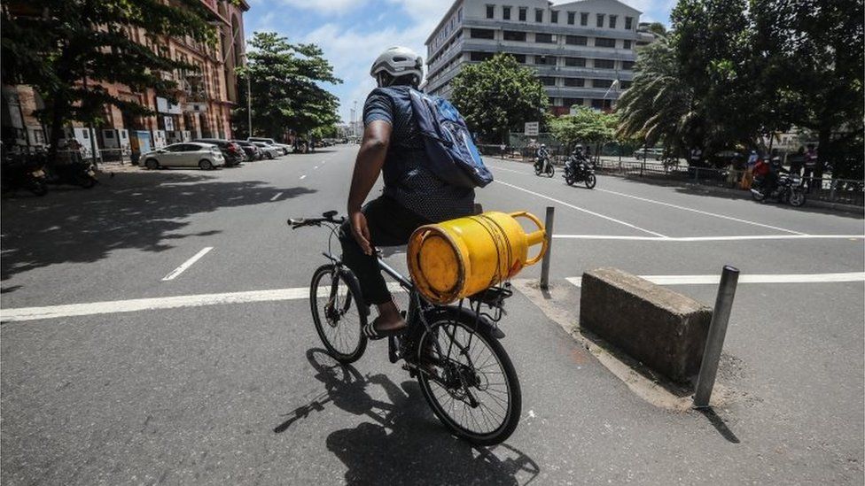 A Sri Lankan man rides a bicycle while he carries an empty cooking gas cylinder on a deserted road amid a fuel shortage in Colombo, Sri Lanka, 29 June 2022