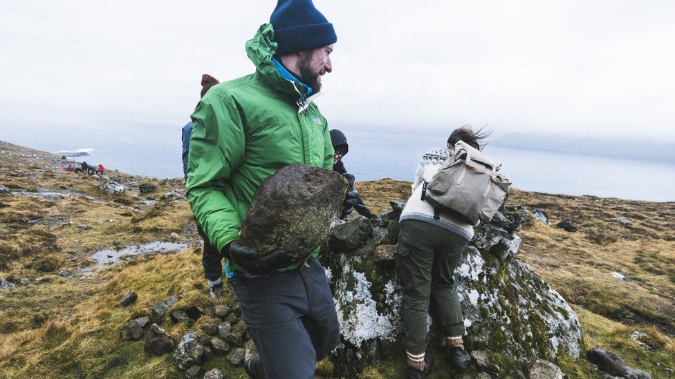 A Brown Team voluntourist carries a big boulder to be placed on a cairn