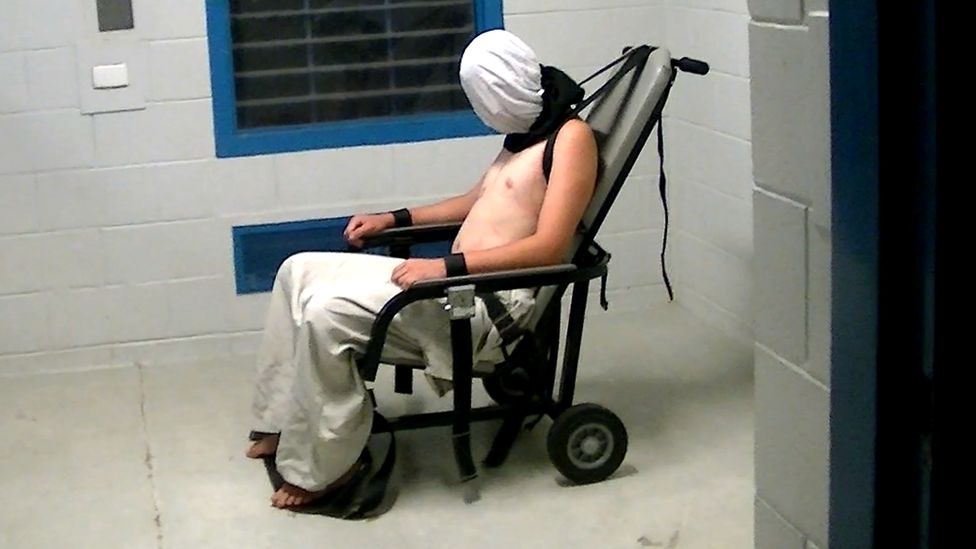 A teenage boy shown hooded and strapped into a chair