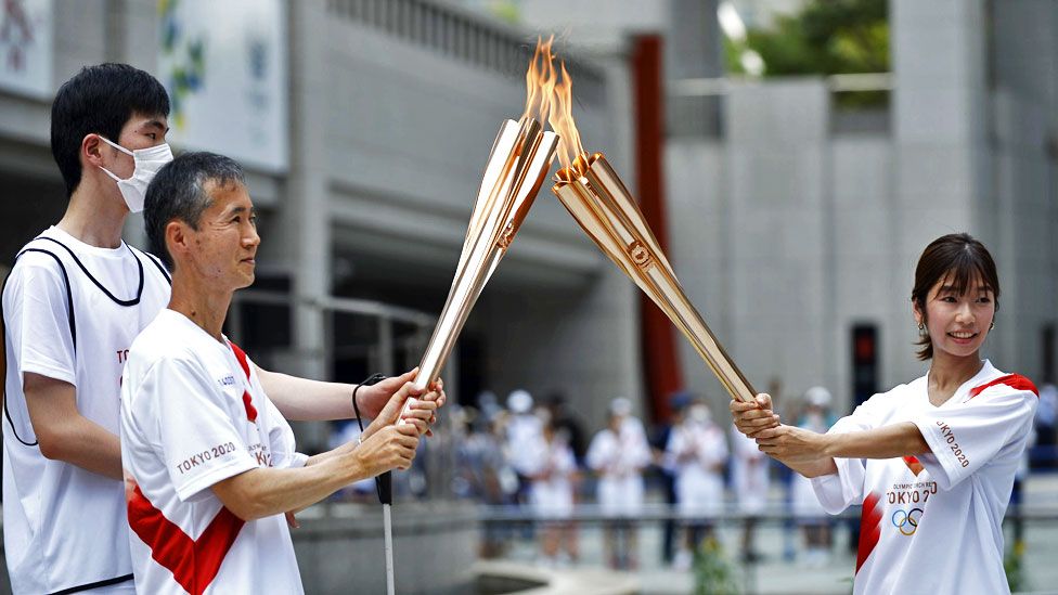 Torchbearers light the Olympic torch and pass the flame around to one another in Shinjuku District in Tokyo, Japan, on 23 July 2021