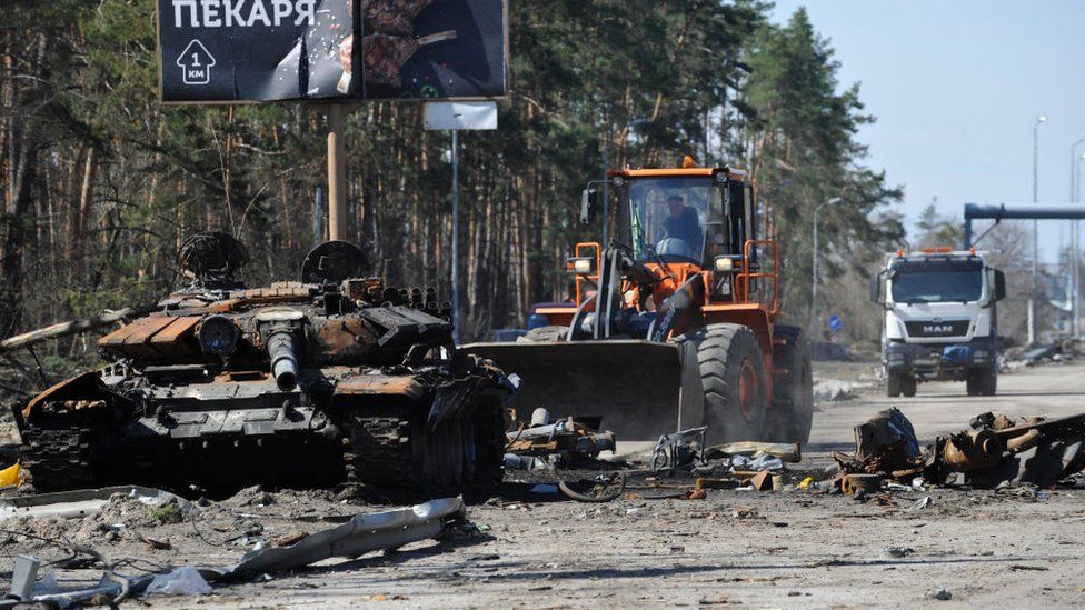 The remnants of a Russian tank is cleared away near Kyiv by a digger