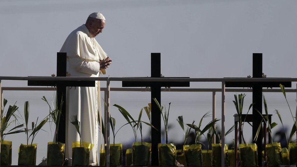 Pope Francis stands on a platform near the US-Mexico border fence