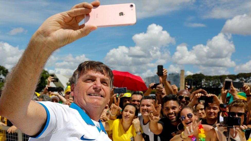 Brazilian President Jair Bolsonaro takes a selfie with supporters in front of the Planalto Palace