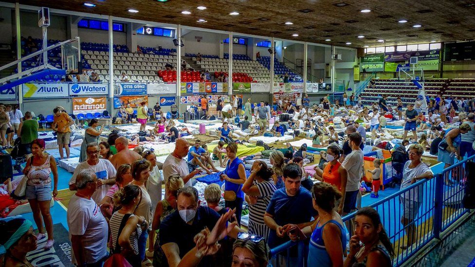 Tourists shelter in a sports hall after being moved away from wildfires in Rhodes