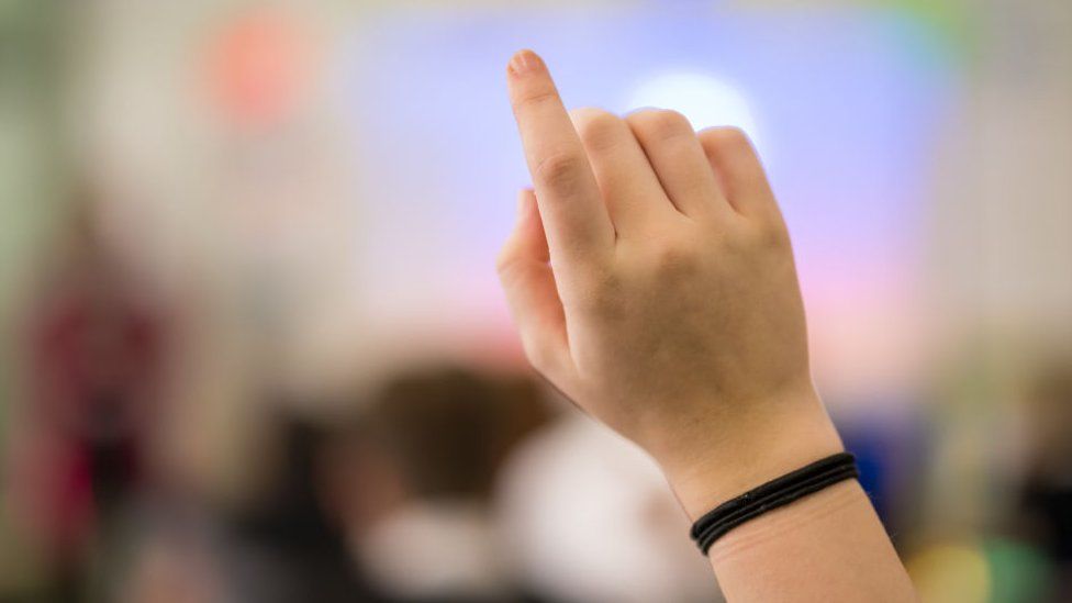 Stock image of a child's hand raised in a school classroom
