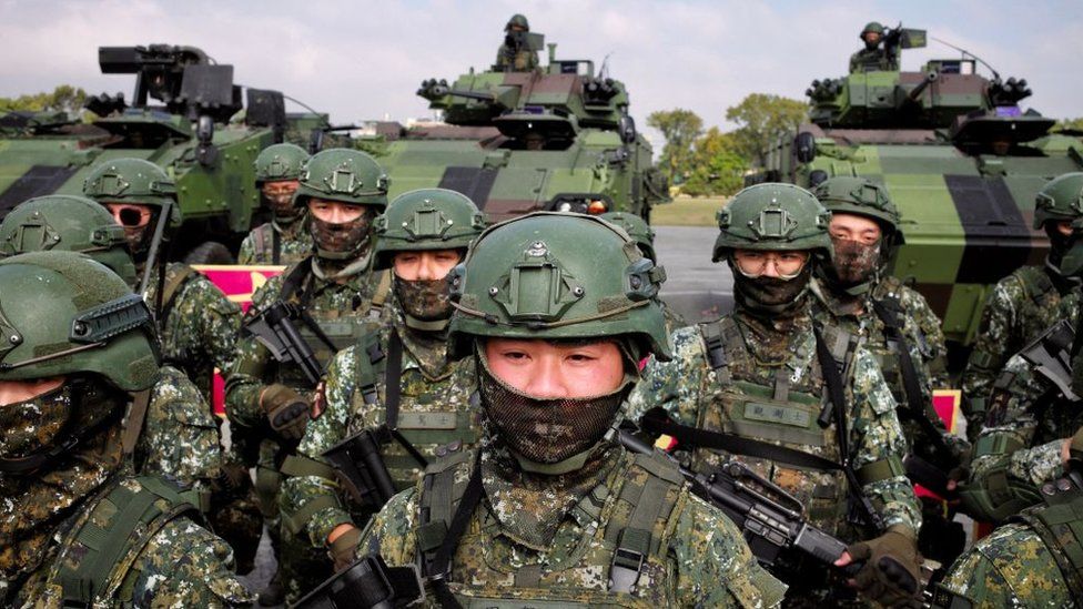 Taiwan soldiers bearing rifles stand at attention in front of tanks.