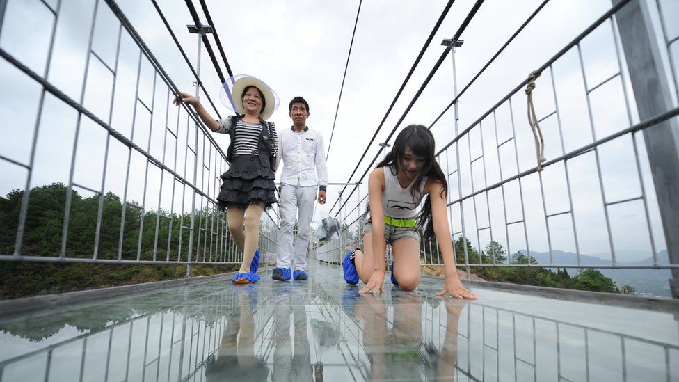 Tourists walk on a suspension bridge made of glass at the Shiniuzhai National Geological Park in Pingjiang County