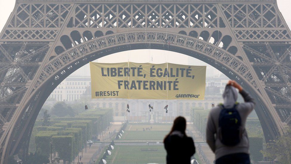 Tourists walk at Trocadero square as activists from the environmentalist group Greenpeace unfurl a giant banner on the Eiffel Tower which reads "Liberty, Equality, Fraternity" in Paris, France (May 5, 2017)