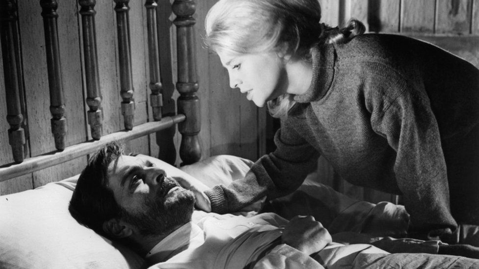 Omar Sharif laying in bed as Julie Christie bends to his bedside to comfort him by touching his cheek in a scene from the film "Doctor Shivago", 1965