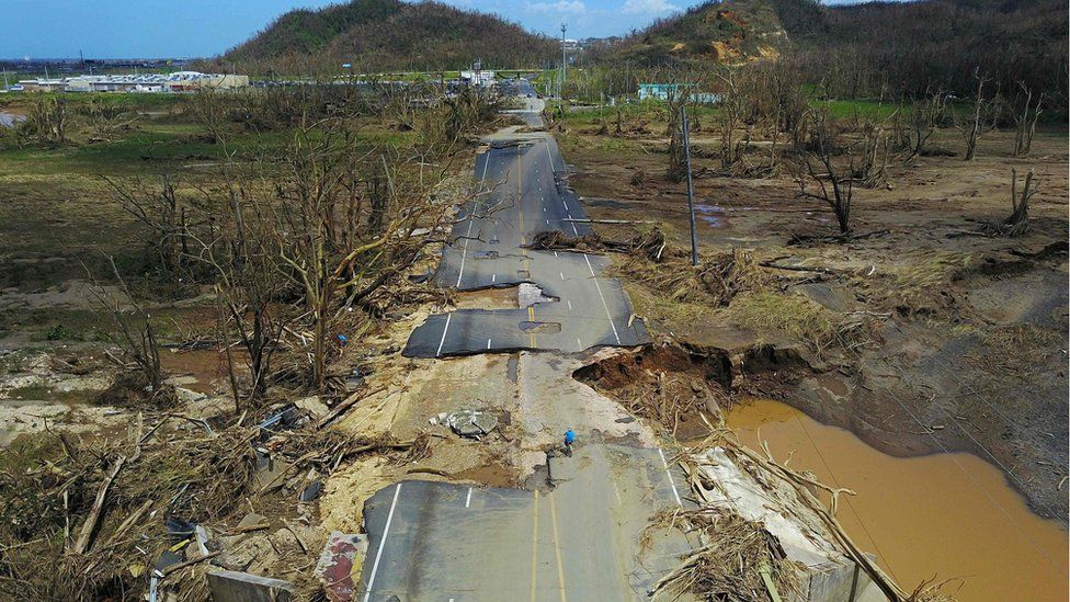 A man rides his bicycle through a damaged road in Toa Alta, west of San Juan, Puerto Rico