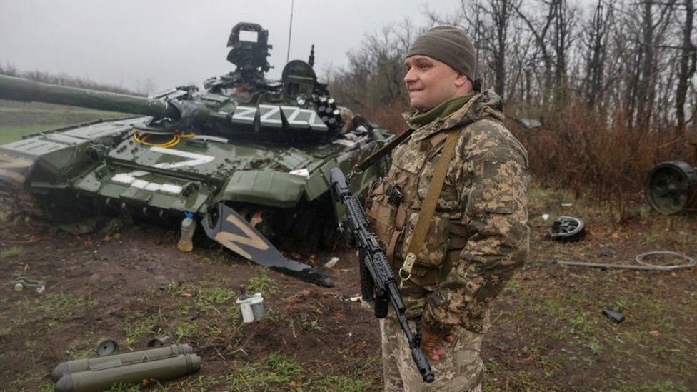 A Ukrainian soldier stands next to a destroyed Russian tank