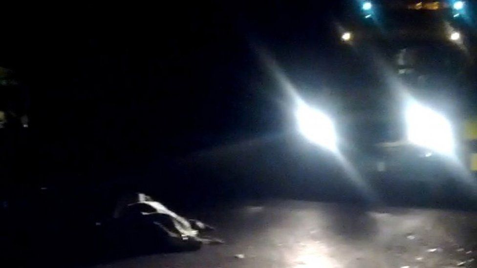 A still image from amateur camera phone video shows a covered body in Weybridge with a police car standing nearby, 10 November