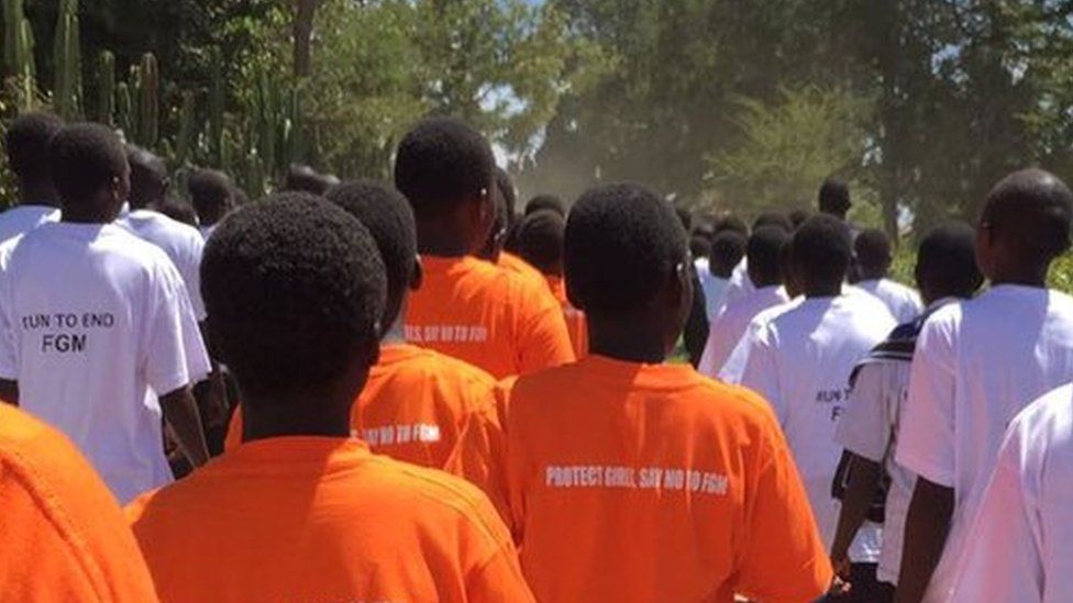 Students walk in a line wearing orange t-shirts that say "Protect girls, say no to FGM" and white t-shirts saying: Run To end FGM