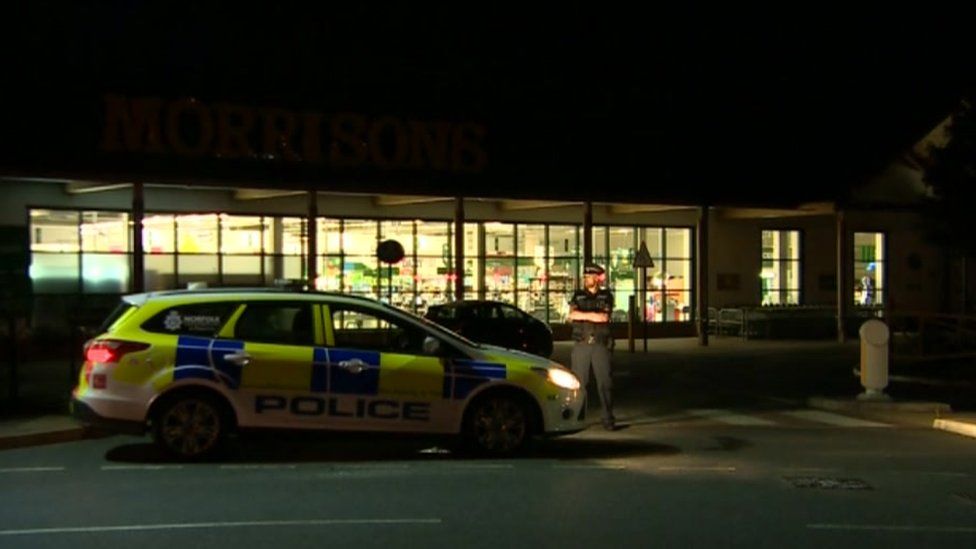 Police officer stands guard next to a police car outside a Norfolk supermarket
