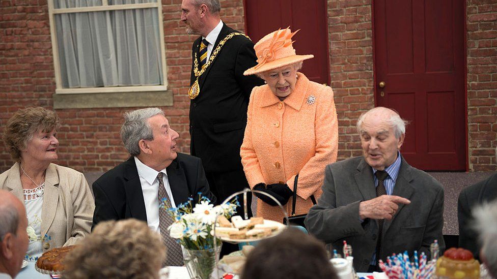 The Queen speaks to people sat at a table for a Jubilee street party in 2012