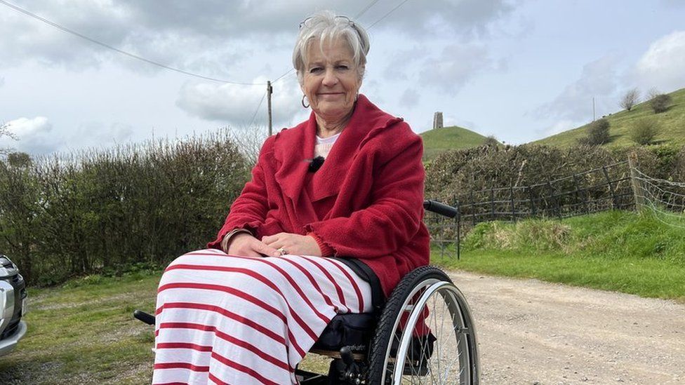 Women smiling sat in a wheelchair in front of Glastonbury Tor