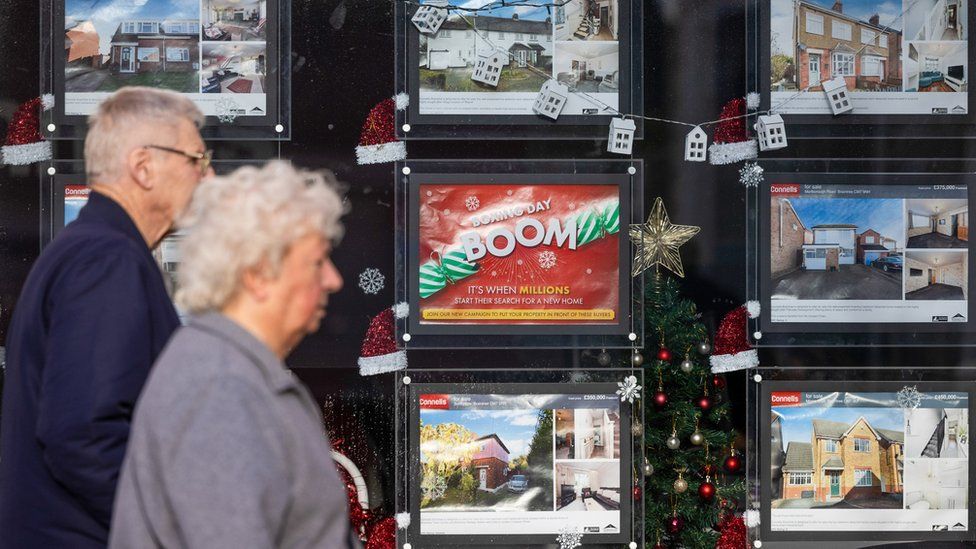 A couple walk past an estate agent's window