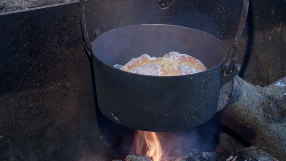 A pot of soda bread cooking over an open fire