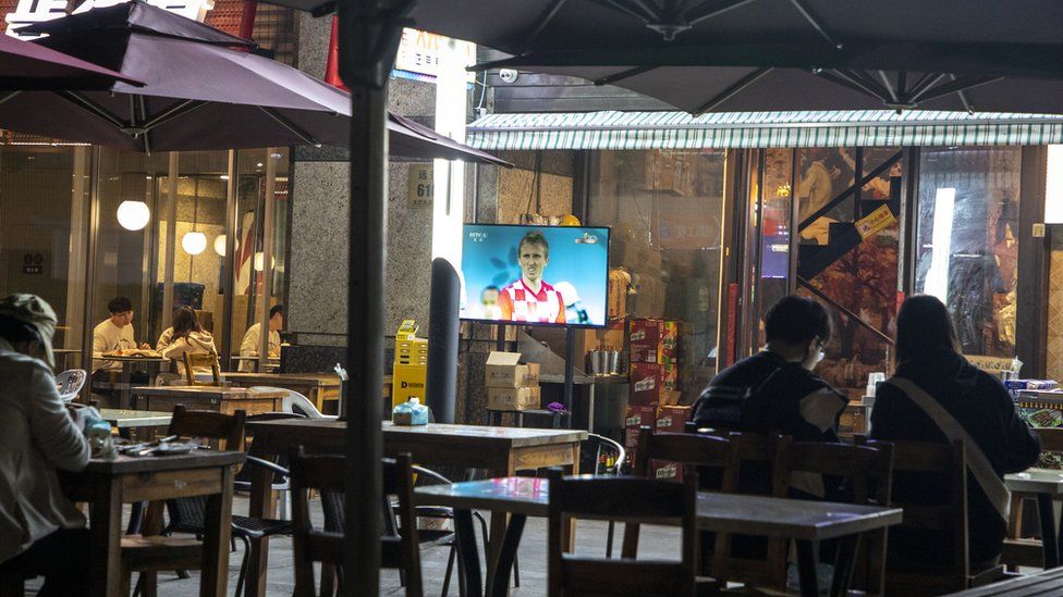 People in Shanghai sitting in a near-empty pub watching a screen showing Croatian footballer Luka Modric
