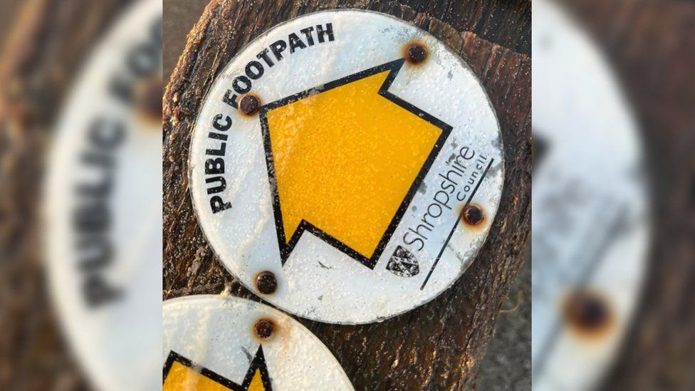 A close up image of the signpost, showing Shropshire Council's logo and a large yellow arrow, signposting which way the footpath is