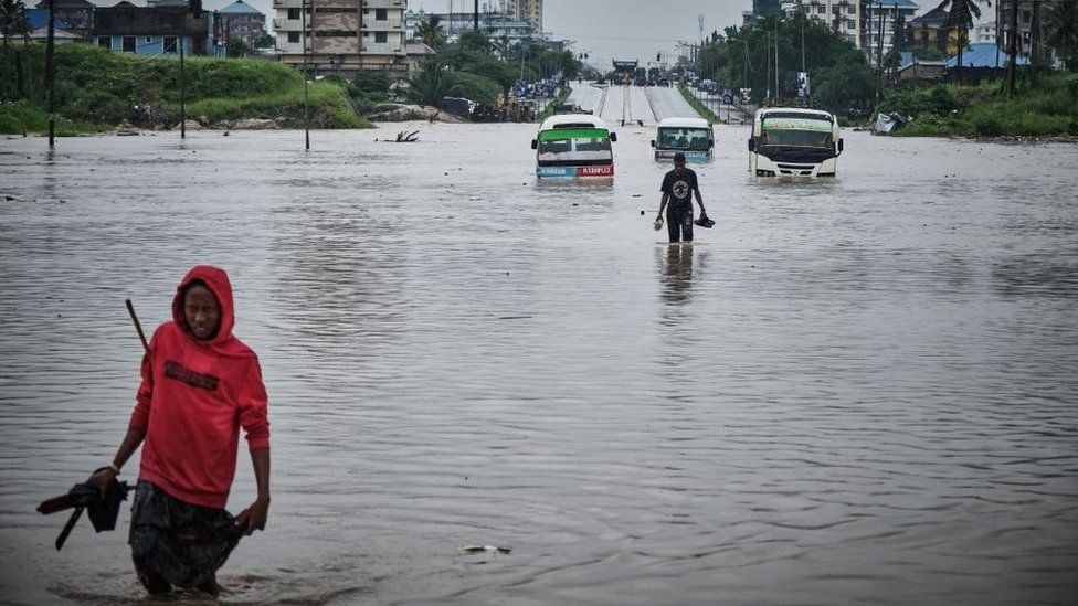 People walk past vehicles stuck in a flooded street in Jangwani, Dar Es Salaam, Tanzania, 25 April 2024