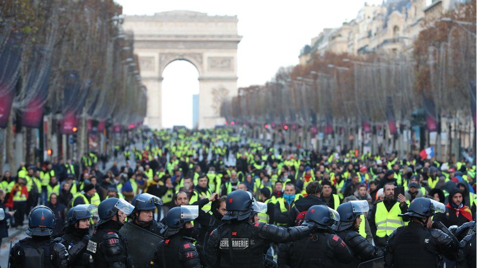 Protesters wearing yellow vests walk on the Champs-Elysees Avenue with the Arc de Triomphe in the background