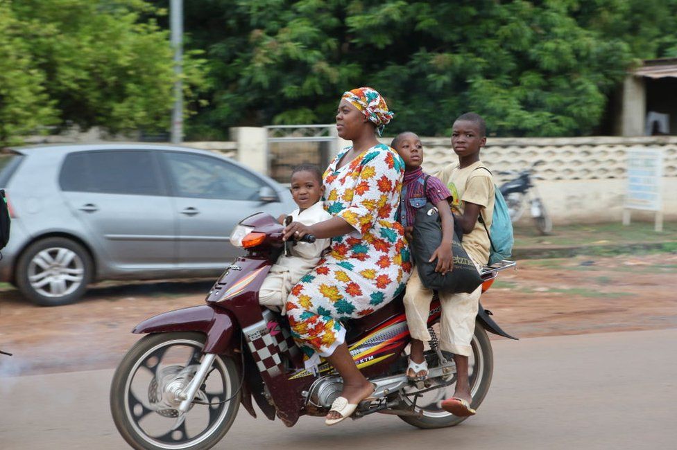 SIKASSO, MALI - JUNE 25: Malian woman rides a motorcycle with her children as daily life amid poverty continues in West African country Mali's Sikasso on June 25, 2022