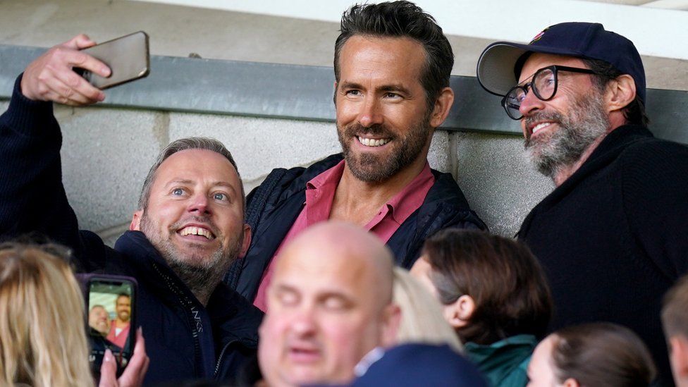 Wrexham Co-Owner, Ryan Reynolds (centre) and Hugh Jackman (right) pose for a photo with a fan