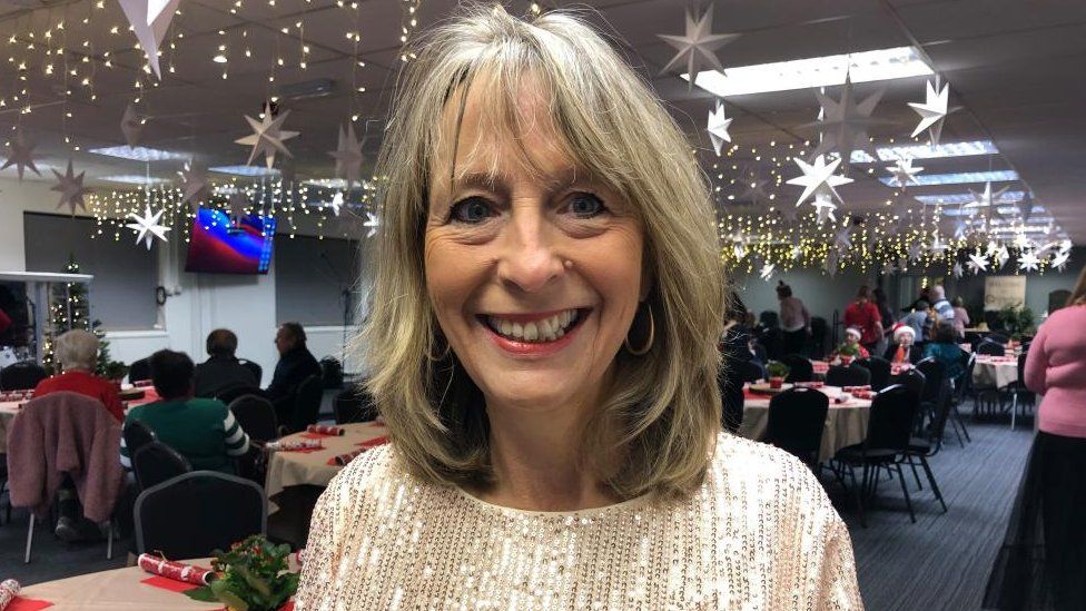 Woman with long blond hair wearing sparkly top in a room full of Christmas decorations