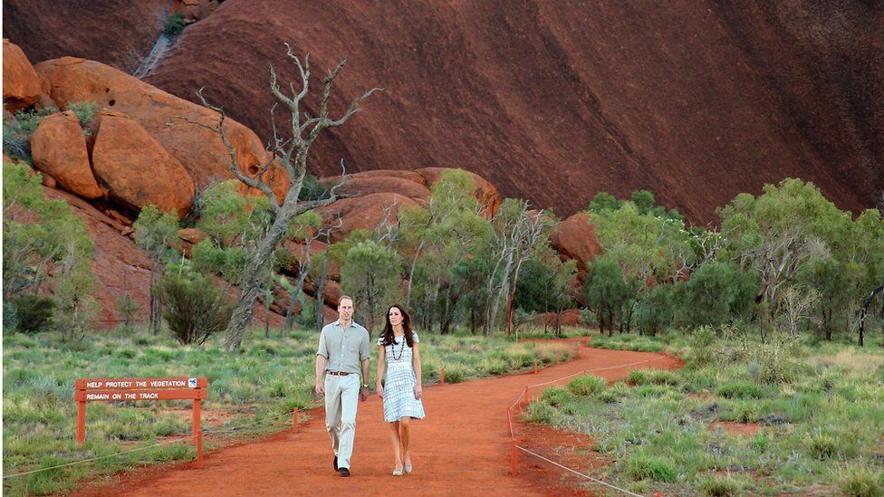 Wide shot of the Duke and Duchess of Cambridge, walking at the base of Uluru