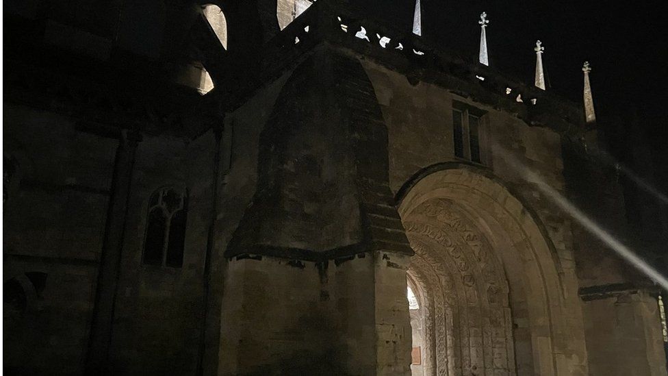 Malmesbury Abbey's porchway, a large archways with carvings, at night with a light shining from inside