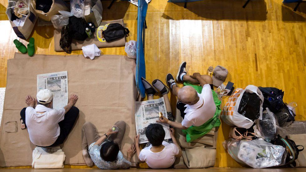 Evacuees read newspapers in a gymnasium used as an evacuation centre on July 9, 2018 in Kurashiki, Okayama