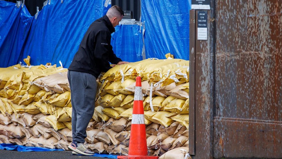 Мужчина складывает мешки с песком, чтобы защитить склад перед приходом циклона Габриэль в Окленде, Новая Зеландия