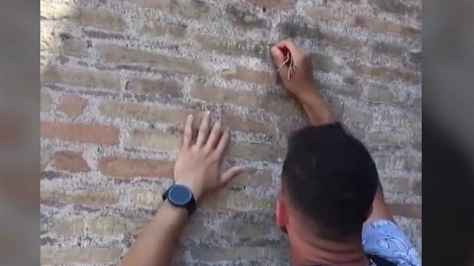 Man carves names onto colosseum wall with a key