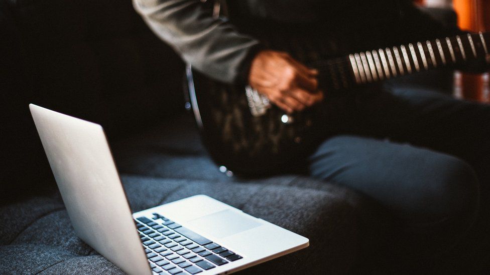 A man playing guitar in front of a laptop