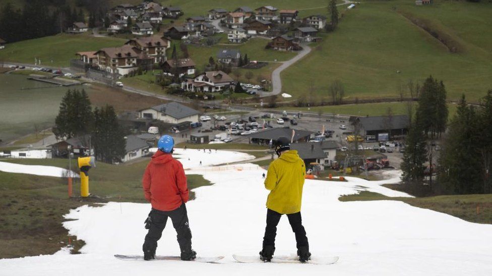 Сноубордисты мчатся по склону с искусственным снегом между Риггисальпом (1491 м над уровнем моря) и Шварцзее Гипсера (1046 м над уровнем моря) в Шварцзее, Швейцария, 30 декабря 2022 г.