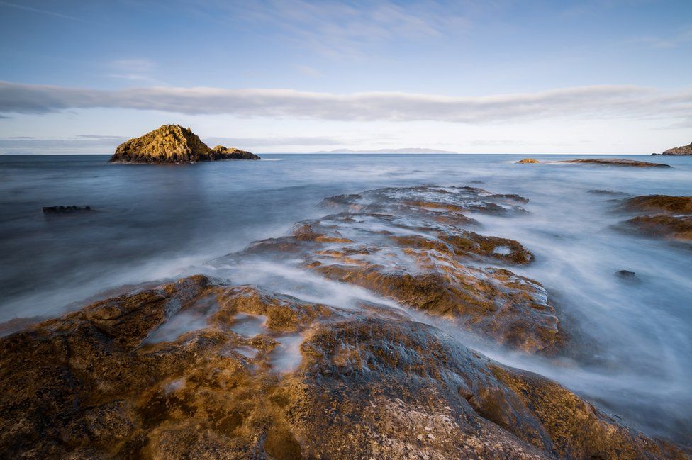 Waves lap over rocks on the beach on a clear, blue-sky day in Newcastle in County Down