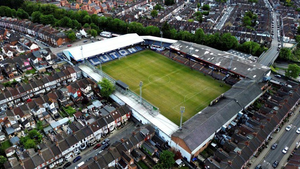 An aerial view of Luton Town's Kenilworth Road stadium. The green grass from the football pitch is visible as well as the four stands which are surrounded by rows of terraced housing.