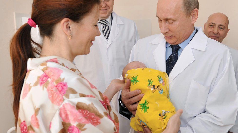 Vladimir Putin holds a baby during a tour of a hospital