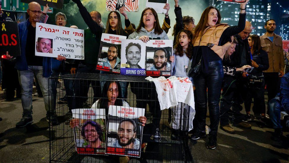A woman sitting in a cage holds posters showing two Israeli hostages still being held by Hamas in Gaza, at a protest in Tel Aviv, Israel (26 March 2024)