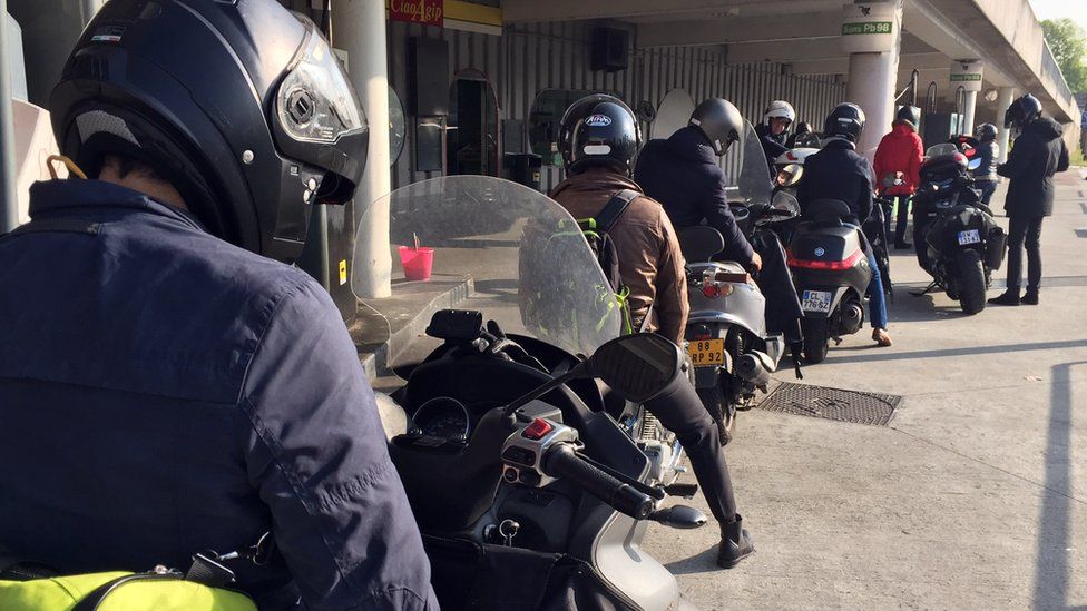 nine motorbike riders queue at a petrol station