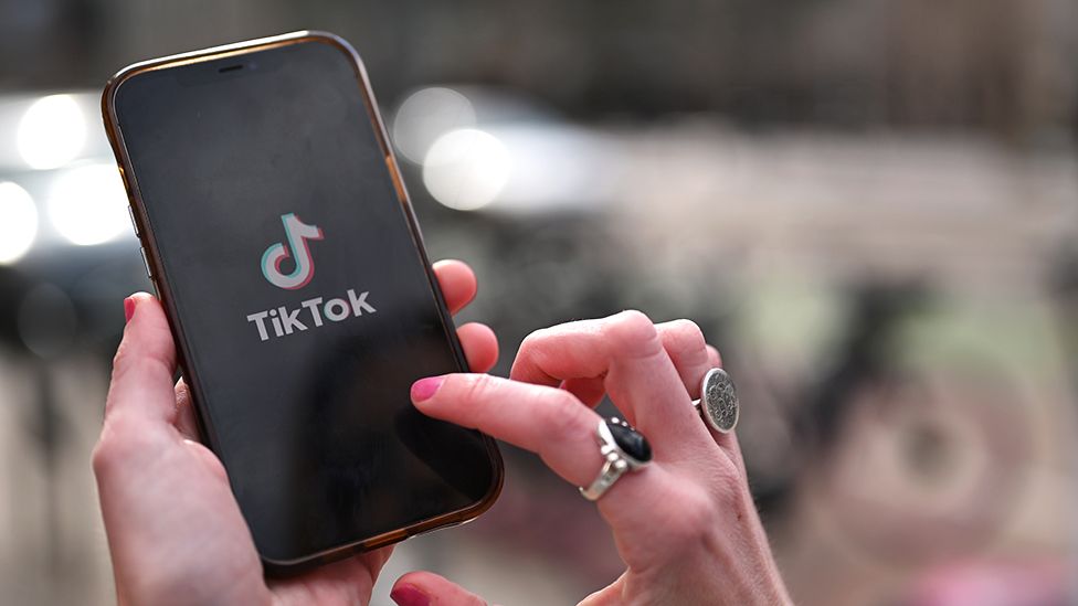 A persons hands use a moblie phone showing the TikTok logo
