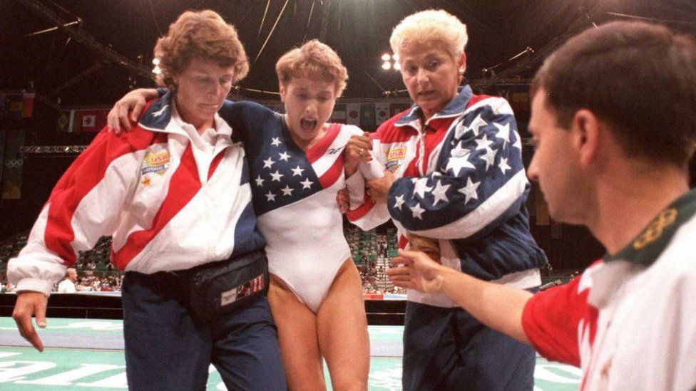 US gymnast Kerri Strug (2nd L) screams in pain as she is carried from the floor by team officials after she injured her ankle at 1996 Olympics