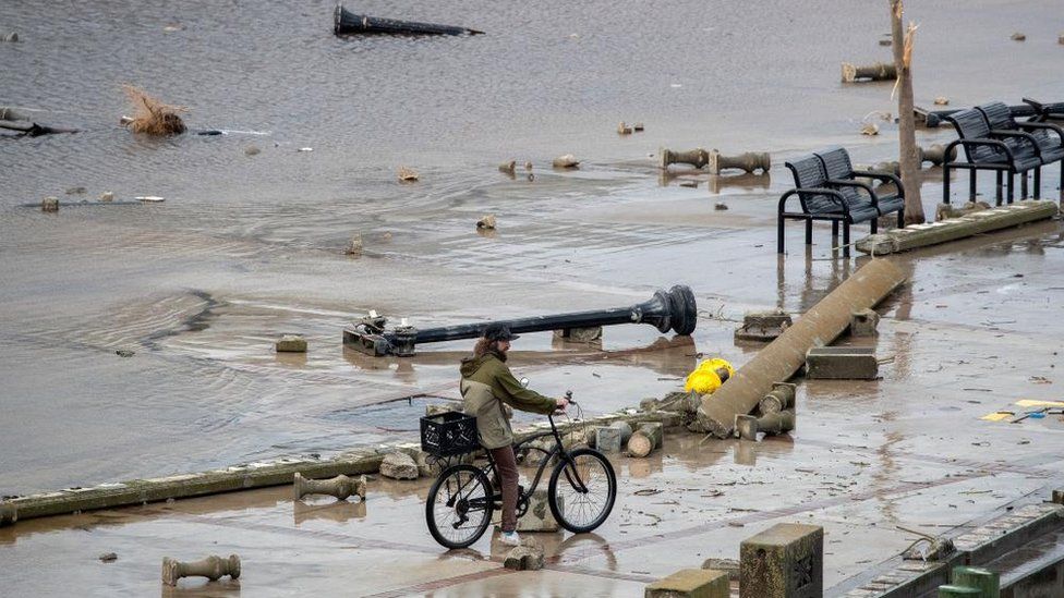Мужчина едет на велосипеде по обломкам наводнения.