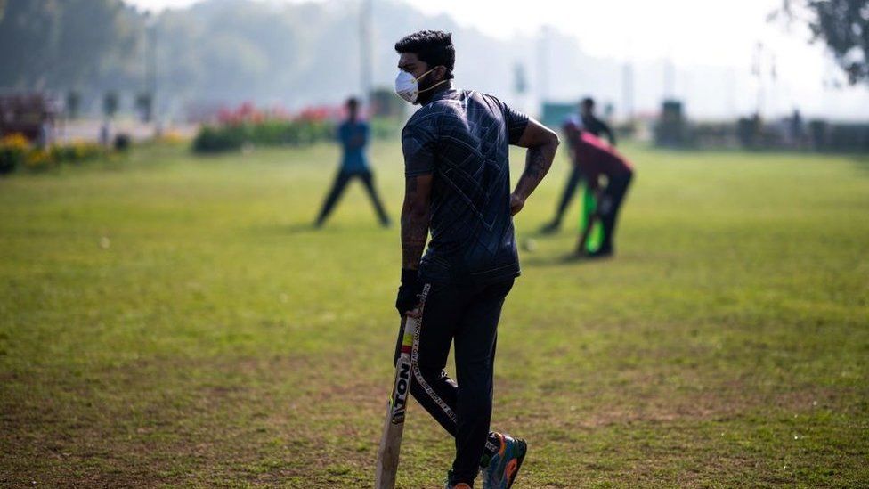 A youth (C) wearing a facemask as a preventive measure against the COVID-19 coronavirus plays cricket with his friends at a park in New Delhi on March 18, 2020.
