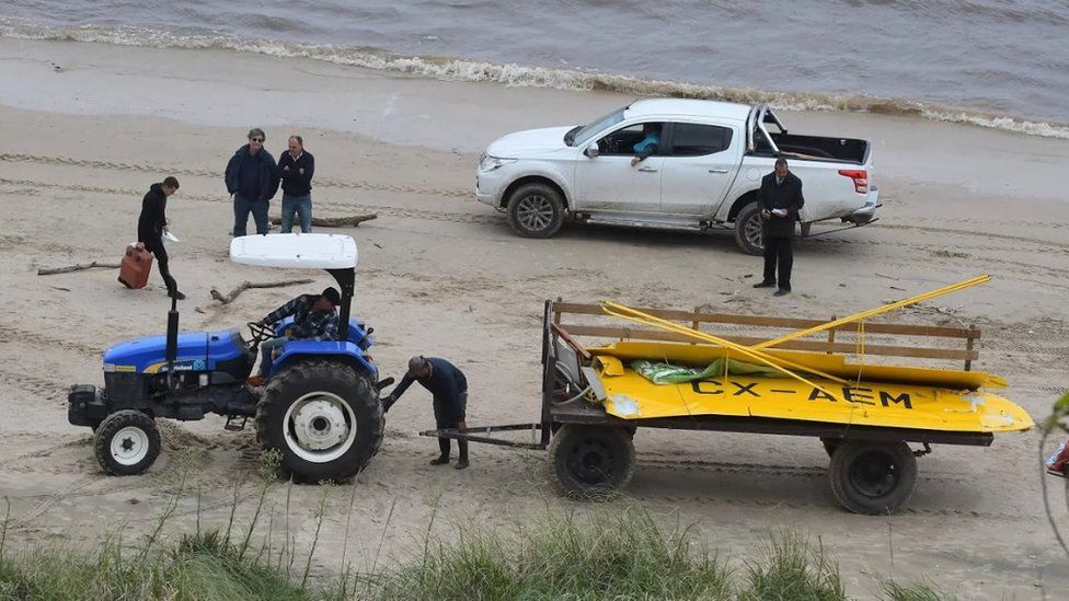 A tractor pulls broken parts of the plane on the beach